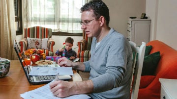 Un hombre teletrabaja desde casa mientras su hijo juega Un hombre teletrabaja desde casa mientras su hijo juega