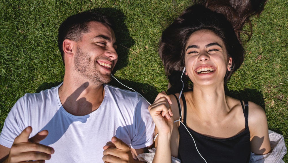 Una pareja comparte sus auriculares tumbada sobre la hierba