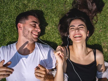 Una pareja comparte sus auriculares tumbada sobre la hierba