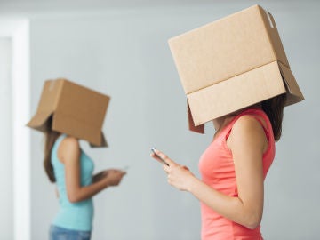Dos jóvenes, aisladas con cajas de cartón en la cabeza, utilizan su teléfono móvil.