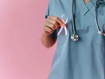 Primer plano de una mano sujetando un lazo rosa, símbolo del cáncer de mama. Primer plano de una mano sujetando un lazo rosa, símbolo del cáncer de mama.