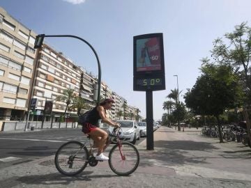 Un ciclista pasa junto a un termómetro que marca 50 grados en Córdoba, en una jornada marcada por la ola de calor que afecta a toda la Península