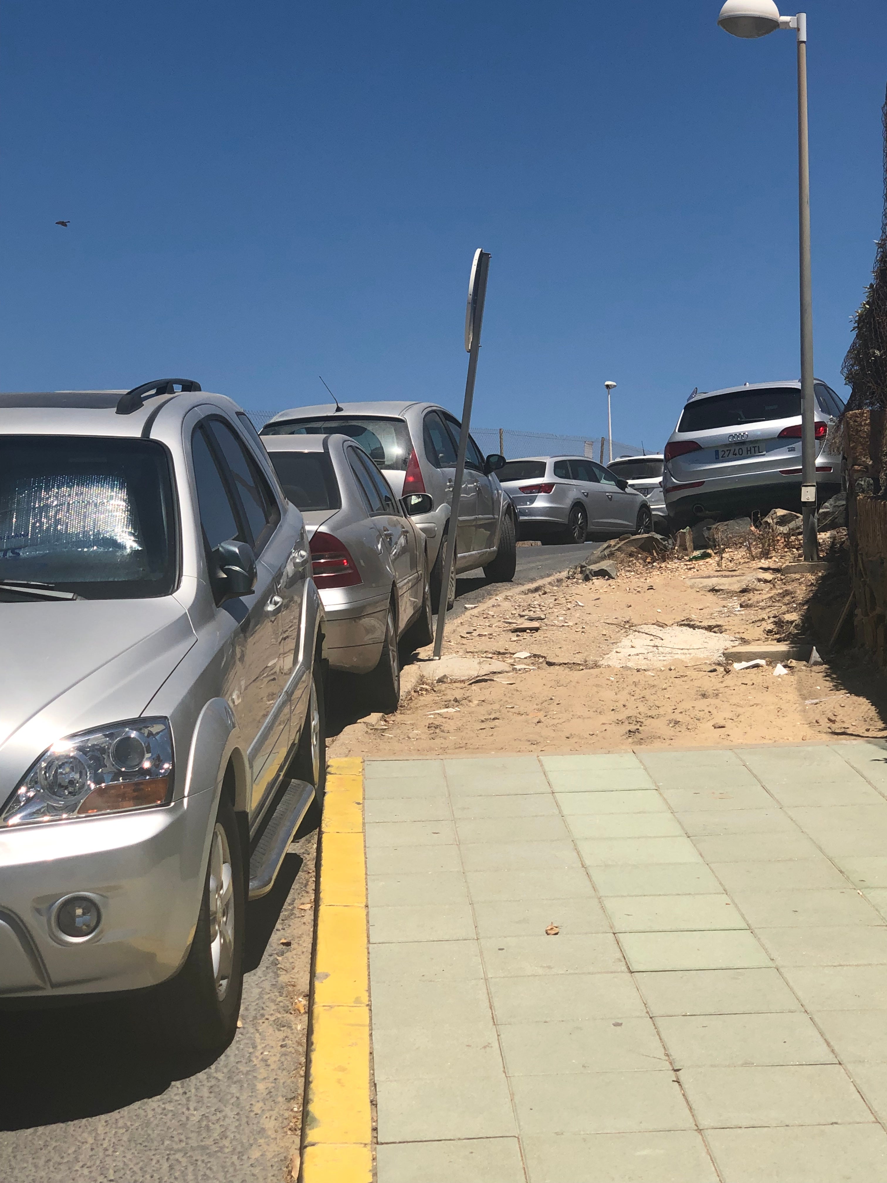 Peligro cada vez que bajamos a la playa Esta es la Avenida de las Arenas, en Punta Umbría, Huelva. Sólo hay un trozo de acera hecha y los coches aparcan formando una línea y bloqueando ambos lados de la calzada, todo el largo. Esta cuesta termina en uno de los accesos a la playa y los peatones nos vemos obligados a subirla y bajarla andando por la calzada y sorteando vehículos tanto aparcados como en circulación.