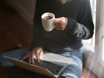 Una mujer bebiendo café y usando el portátil