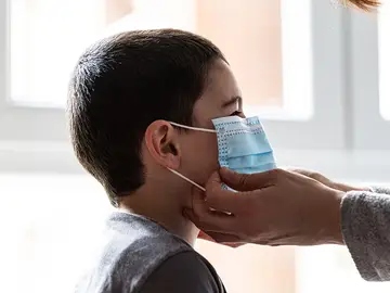 Una mujer coloca una mascarilla a un niño Una mujer coloca una mascarilla a un niño