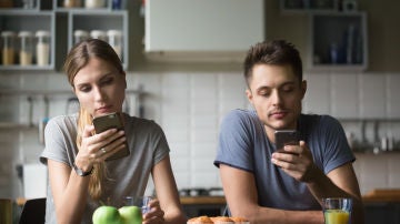 Dos jóvenes desayunando miran atentamente sus móviles.