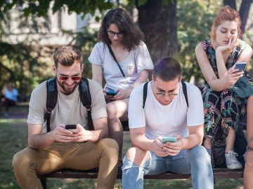 Grupo de amigos sentado en un banco miran sus móviles