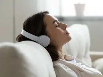 Mujer escucha tranquilamente sus auriculares en el sofá Mujer escucha tranquilamente sus auriculares en el sofá