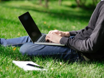 Una persona sentada en un prado navega por Internet con un portátil