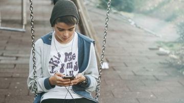 Un niño consulta su móvil en un parque Un niño consulta su móvil en un parque