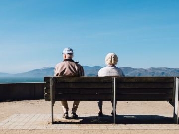 Dos ancianos sentados en un banco mirando hacia el horizonte costero