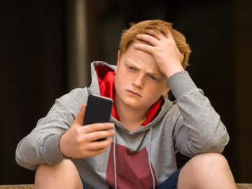 Un adolescentes preocupado mira su móvil.