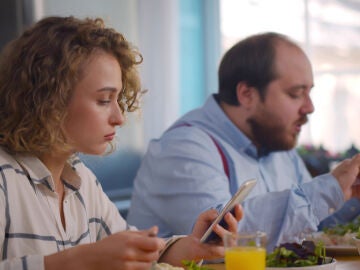 Una pareja come y mira el teléfono móvil a la vez.