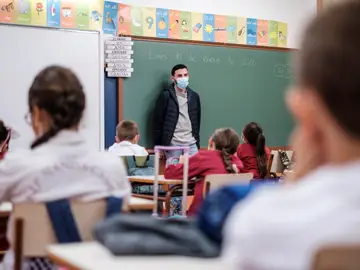 Un profesor da clase con mascarilla a un grupo de niños Un profesor da clase con mascarilla a un grupo de niños
