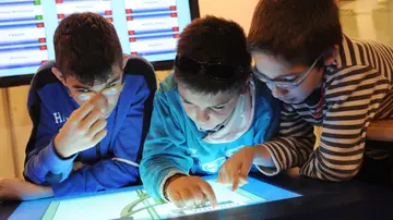 Tres niños con una discapacidad visual consultan un ordenador accesible.