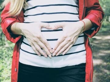 Una mujer embarazada hace la forma de un corazón con sus manos sobre su vientre.