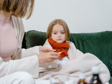 Un momento cari&ntilde;oso de una mujer revisando la temperatura de un ni&ntilde;o enfermo en un acogedor sof&aacute; verde en interiores