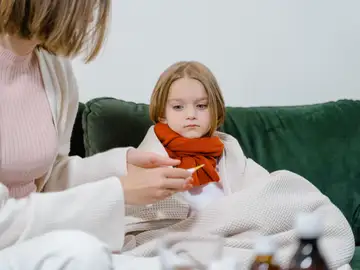 Un momento cariñoso de una mujer revisando la temperatura de un niño enfermo en un acogedor sofá verde en interiores Un momento cariñoso de una mujer revisando la temperatura de un niño enfermo en un acogedor sofá verde en interiores