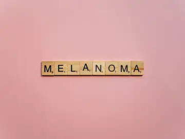 Letras de Scrabble de madera escribiendo 'Melanoma' sobre un fondo rosa suave, simbolizando la concienciación. Letras de Scrabble de madera escribiendo 'Melanoma' sobre un fondo rosa suave, simbolizando la concienciación.